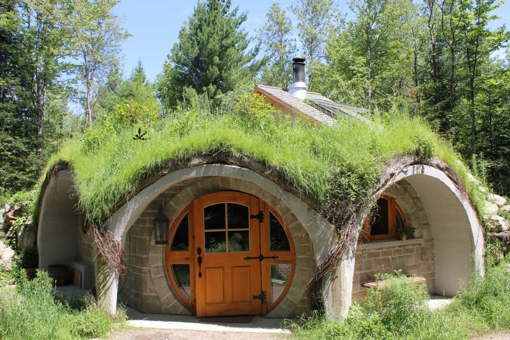 Photo of a modern Hobbit-style house rental property in Quebec. Rounded roof with grass on top, with large round door