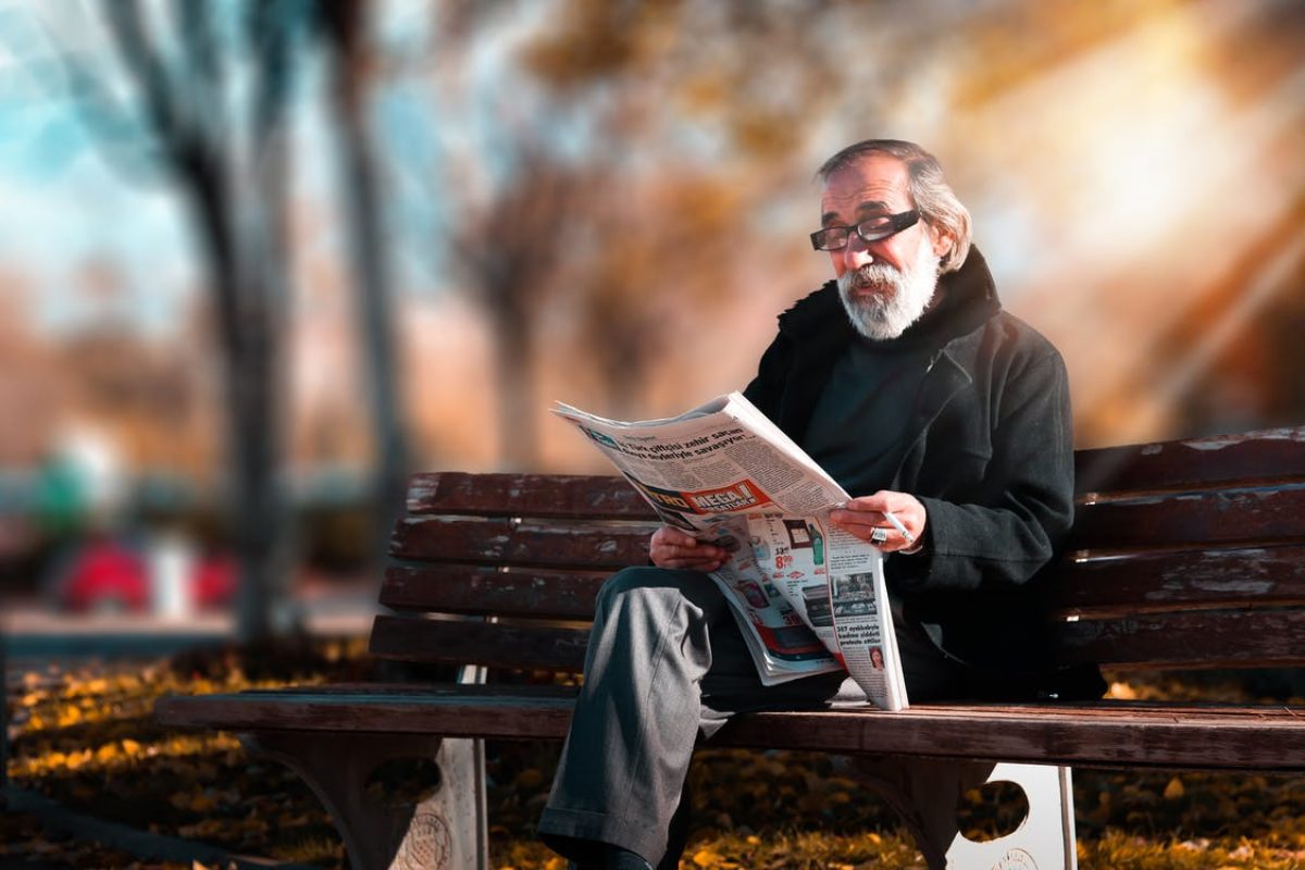 senior man reading newspaper on a bench in a park